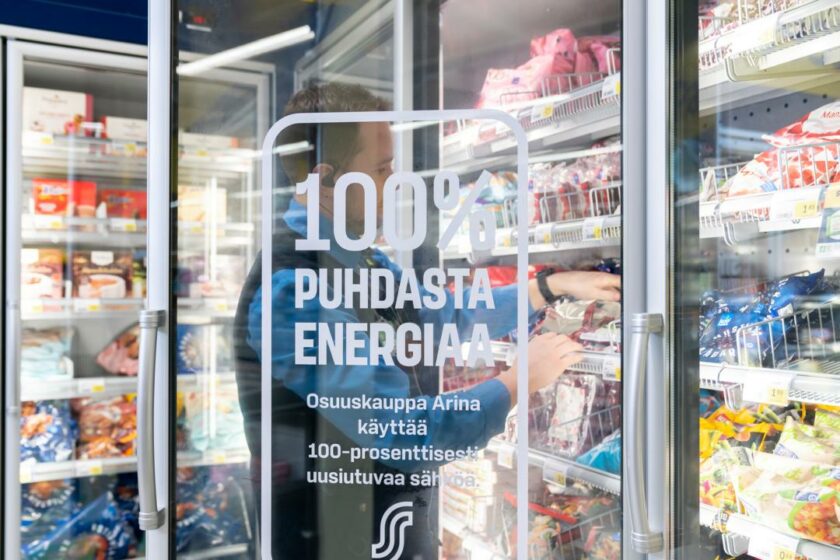 Kuvassa Osuuskauppa Arinan myyjä seisoo avatun kylmäkaapin ovella. Ovessa teksti 100% puhdasta energiaa.