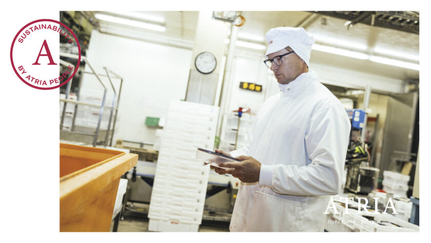 Atrian tehdastiloissa valkopukuinen ja -hattuinen työntekijä seisoo ja katsoo kädessään olevaa padia.